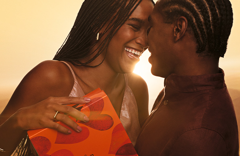 Pareja sonriendo mientras intercambia un regalo en un momento de celebración y cariño.